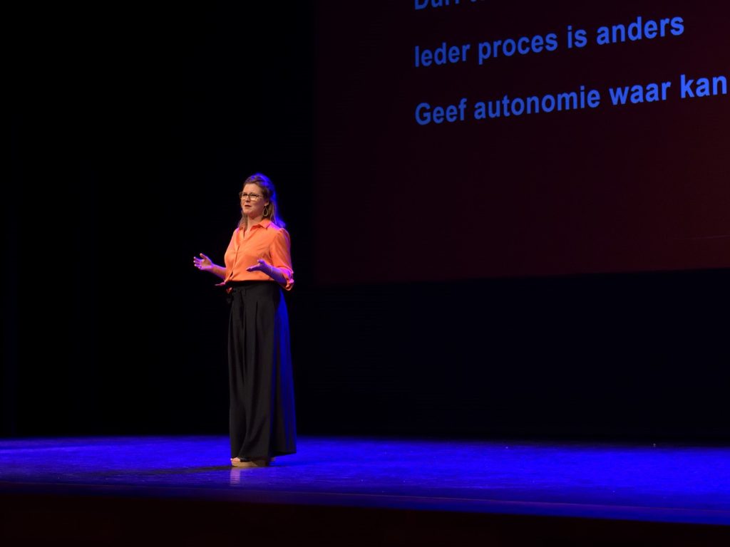Marieke legt uit als spreker tijdens congres op podium